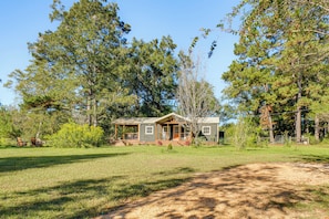 A rustic cabin with a porch, surrounded by a grassy yard and tall trees. - On 80 Acres! Serene Orchard Farm Stay in Lumberton (Lumberton)