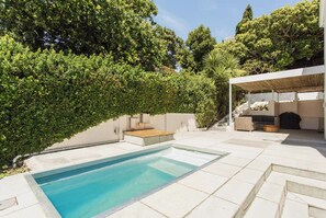 A swimming pool with a tiled deck, surrounded by lush greenery and a covered outdoor seating area. - Green Point Town Haus (Cape Town)