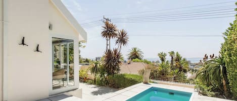 A residential property with a swimming pool, a glass door entrance, and a view of the sea.