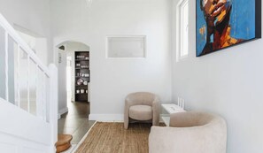 A hallway with a staircase, a beige armchair, a rug, and a painting on the wall. - Green Point Town Haus (Cape Town)