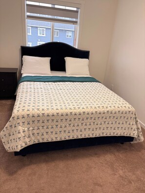 A bed with a patterned bedspread, a dark headboard, and a window with a view of buildings. - SpaciousCalgaryHome l 4 Bedrooms l Sleeps 8 plus (Calgary)