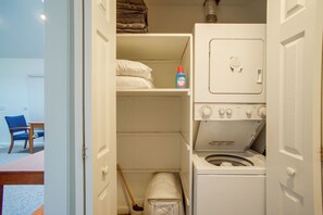 Een wasserette met een voorlader wasmachine en droger, een plank met opgevouwen handdoeken, en een fles wasmiddel.