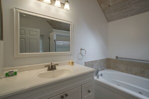 Ein Badezimmer mit einem weißen Waschbecken, einem großen Spiegel, einer Badewanne und einem Handtuchhalter.