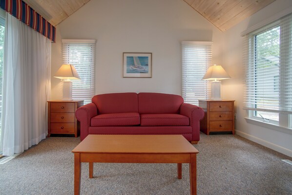 A cozy room with a red sofa, two nightstands with lamps, a wooden table, and a framed picture on the wall. - Retreat 2 Mi to Cape Cod Beaches! Bring Your Pets (Mashpee)