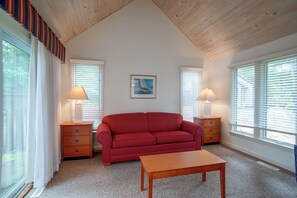 Uma sala de estar aconchegante com um sofá vermelho, duas mesas laterais com abajures, uma mesa de centro de madeira e um quadro emoldurado na parede.