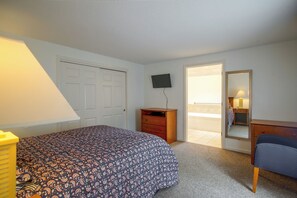 Ein Schlafzimmer mit Bett, Kommode, Fernseher und einer Tür zu einem Balkon.