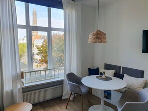 A modern room with a round white table, two grey chairs, a white radiator, and a view of a tower through large windows. - "Mien lüttje Lichtblick" Vacation Rental—freshly renovated with a view of the (Borkum)