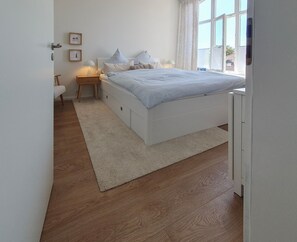 A bedroom with a bed, bedside tables, a nightstand, a window, and a door. - "Mien lüttje Lichtblick" Vacation Rental—freshly renovated with a view of the (Borkum)