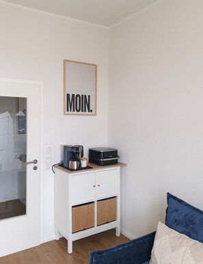 Una habitación con un armario blanco, una cafetera y un tostador encima. En la pared hay un letrero enmarcado que dice 'MOIN'.