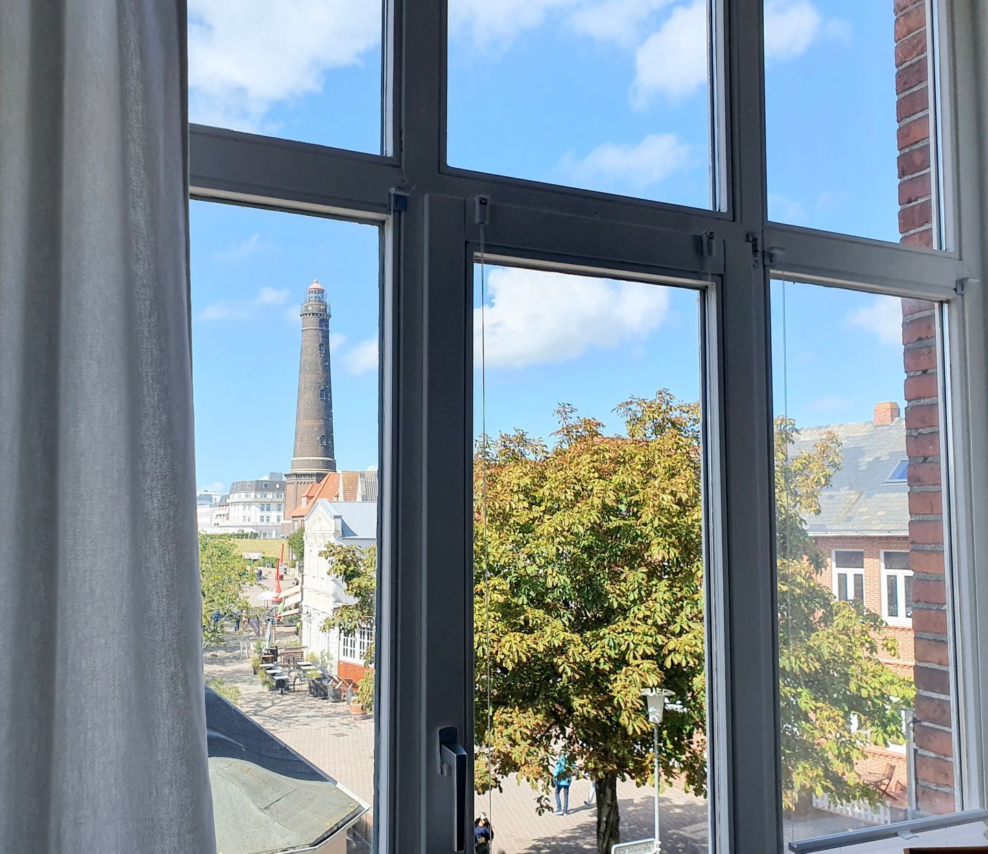 A window with a view of a tall chimney, a tree, and buildings in the background.