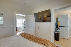 Quarto com cama, televisão fixada na parede e corredor que dá para um banheiro.