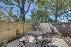 Eine Terrasse mit einem runden Metalltisch und vier Stühlen, umgeben von einem Holzzaun und Bäumen.
