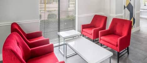 A modern interior with red upholstered chairs, a white table, and a large window with blinds.