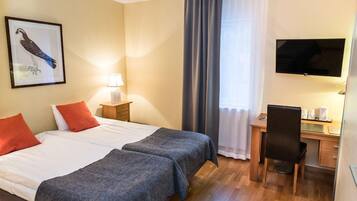 Et hotelværelse med to senge, et skrivebord, en stol, et fjernsyn og et billede i ramme på væggen.