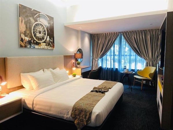 Una habitación de hotel con una cama grande, una mesita, una silla y un ventanal con cortinas.