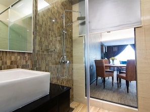 Un baño moderno con una bañera blanca grande, un box de ducha con mampara de vidrio y vistas a un comedor a través de una puerta de cristal.
