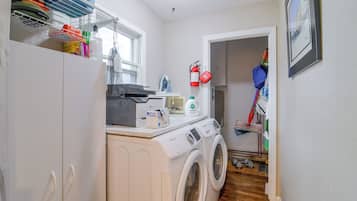 Une buanderie équipée d’un lave-linge, d’un sèche-linge, d’une planche à repasser et de divers produits de nettoyage.
