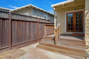 A residential property with a wooden deck, a concrete patio, and a house with a beige exterior and a brown door. - 1 Mi to Beach, Walk to Restaurants Cozy Home (Alameda)
