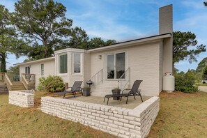 A single-story house with a covered patio, two windows, a chimney, and a small staircase leading to a deck. - White Heron Landing - Waterfront New Bern Home! (New Bern)
