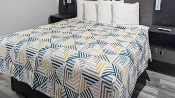 A neatly made bed with a geometric patterned bedspread, a headboard, and bedside tables with lamps.