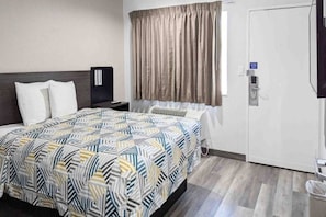 Habitación de hotel con cama, mesita de noche, ventana con cortinas, puerta y televisor montado en la pared.