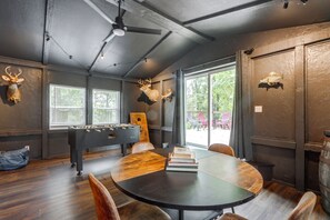 Une pièce avec une table ronde, des chaises, un baby-foot et des têtes d’animaux fixées au mur.