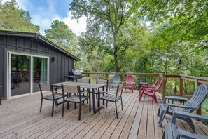 Eine Holzterrasse mit Tisch und Stühlen, einem Grill und Adirondack-Stühlen.
