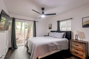 Une chambre à coucher avec un lit, une table de chevet, un ventilateur de plafond et une fenêtre avec des rideaux.