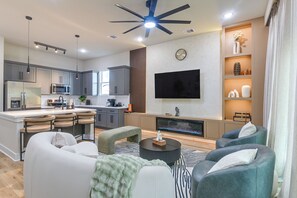 Ein modernes Wohnzimmer mit Kamin, einem flachbildfernseher an der Wand und einer Sitzecke mit Sofas und Sesseln.