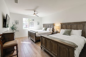 A bedroom with two wooden beds, a desk, a chair, a ceiling fan, and a window with a view of houses. - Large Patio Oasis, Games, Pool! Indio Getaway (Indio)