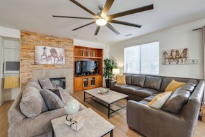 A living room with a stone wall, a fireplace, a television, a leather sofa, and a globe on a coffee table. - Large Patio Oasis, Games, Pool! Indio Getaway (Indio)