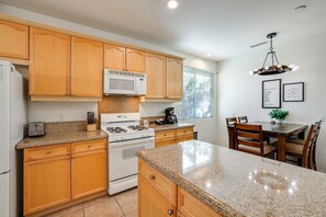 A kitchen with wooden cabinets, a microwave, a stove, and a dining area with chairs and a table. - Large Patio Oasis, Games, Pool! Indio Getaway (Indio)