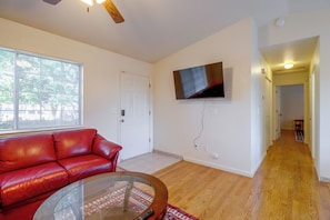 A living room with a red leather sofa, a glass coffee table, a flat-screen TV mounted on the wall, and hardwood flooring. - 37 Min to Tesla Gigafactory! Sun Valley Home (Sun Valley)
