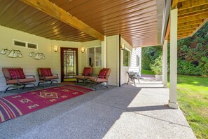 A covered porch with seating, a patterned rug, and a view of the surrounding greenery. - Snohomish Executive Suite w/ Deck & Fire Pit (Snohomish)