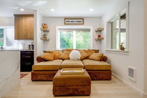 A modern living room with a sectional sofa, a coffee table, and a kitchen area with cabinets and a window. - Snohomish Executive Suite w/ Deck & Fire Pit (Snohomish)