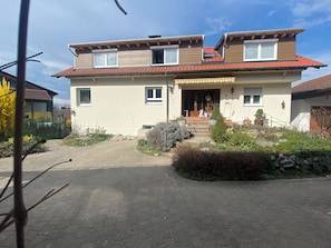 A two-story house with a red-tiled roof, a front porch, and a garden with various plants. - Idyllic vacation rental with a south-facing balcony for up to 6 people (Lindau (Bodensee))