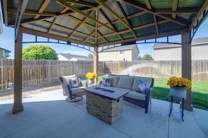 Ein überdachter Patio-Bereich mit einem Steintisch, Korbmöbeln und gelben Blumen.