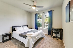 Ein Schlafzimmer mit einem Bett, einem Schreibtisch, einem Stuhl, einem Deckenventilator und einem Fenster mit Vorhängen.