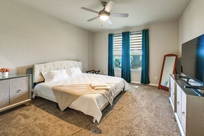 Ein Hotelzimmer mit Bett, Nachttisch, Kommode, Deckenventilator, Fenster mit Vorhängen und einem Fernseher.