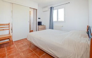 A bedroom with a bed, a wooden chair, a bedside table with a lamp, a window with curtains, and an air conditioning unit. - Beautiful apartment in Folelli with WiFi (Folelli)