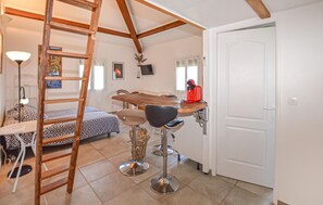 Een kamer met een houten ladder, een bed met behang, een eettafel met stoelen en een rode koffiezetapparaat.