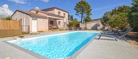 A swimming pool with lounge chairs and a building with a tiled roof.