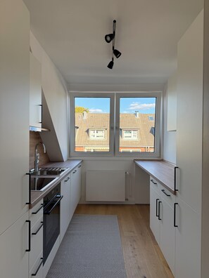 A modern kitchen with a built-in oven, a sink, and a window overlooking a residential area. - New & cozy in the heart of the city (Hamburg)