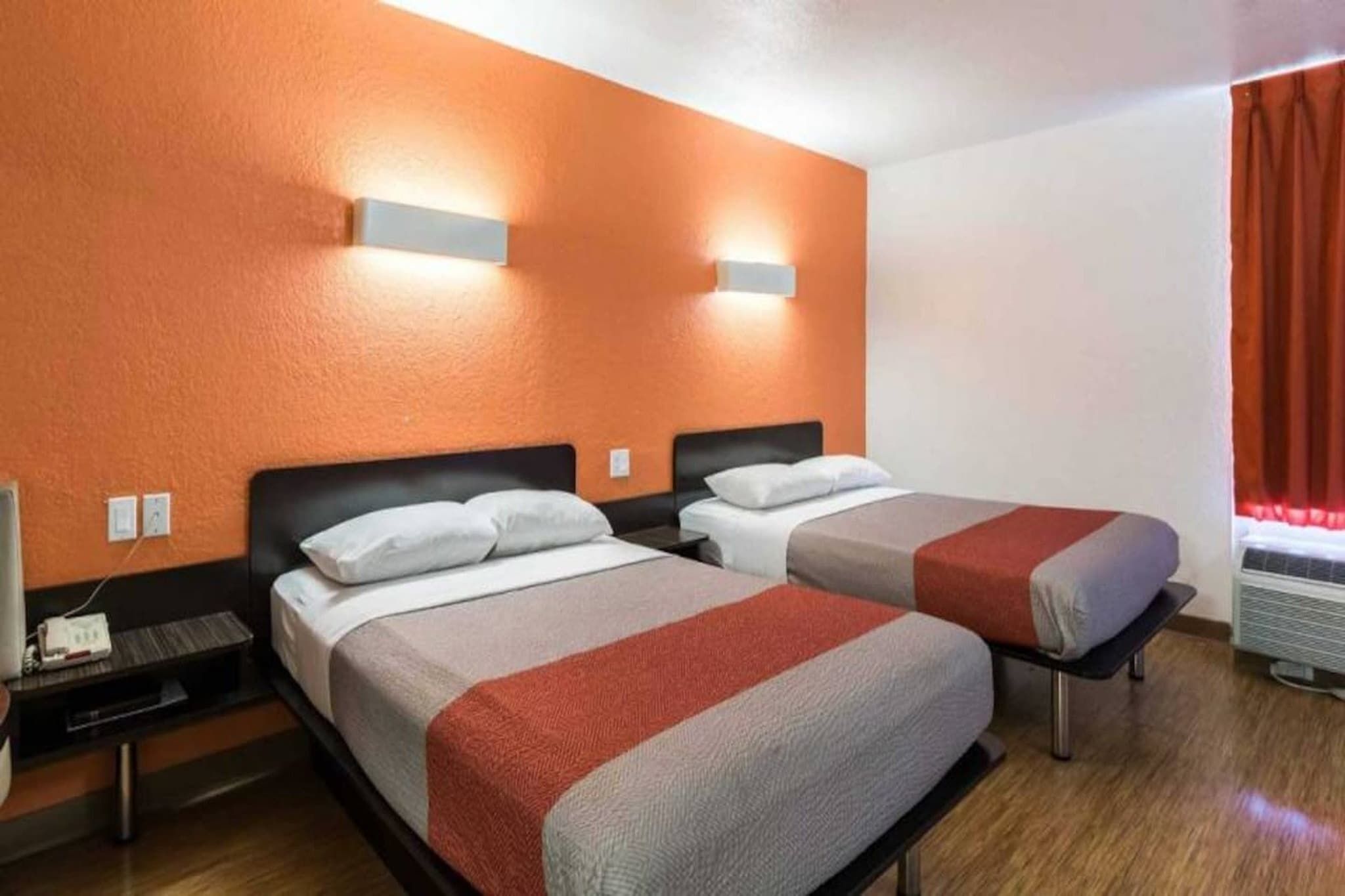 A hotel room with two beds, a nightstand, a heater, and a window with curtains.