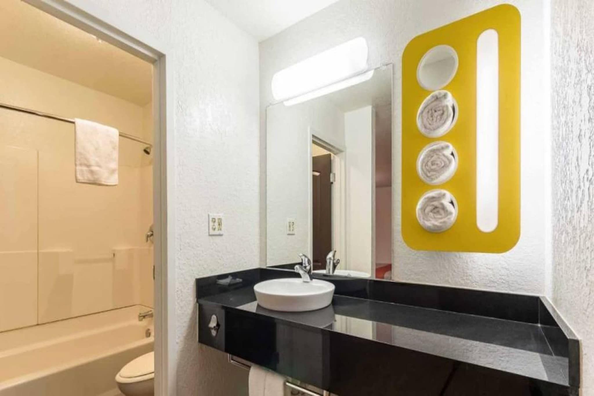 A modern bathroom with a black countertop, a white sink, and a mirror with a yellow light fixture.