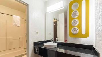 A modern bathroom with a black countertop, a white sink, and a mirror with a yellow light fixture.
