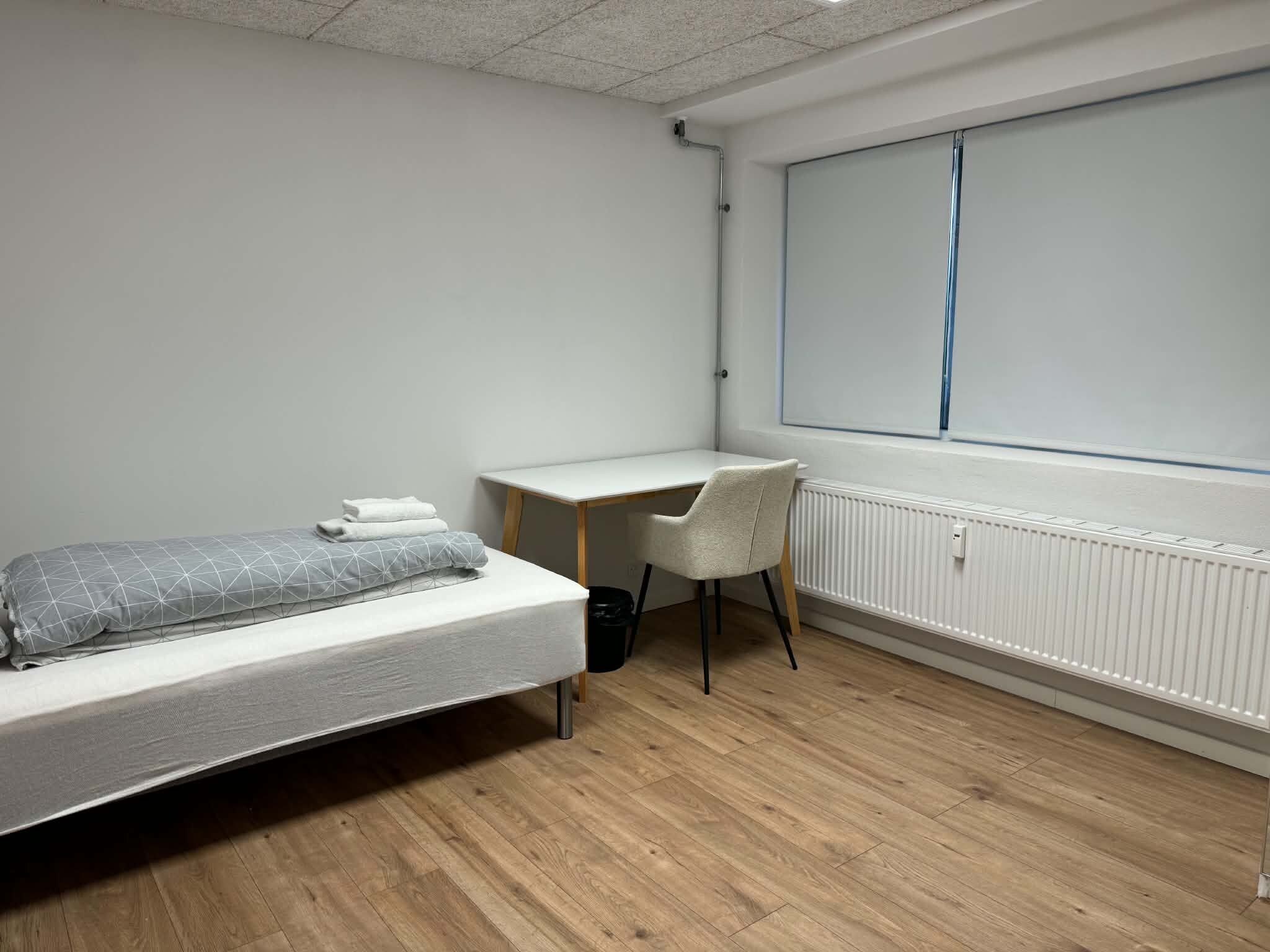 A bedroom with a bed, a desk, a chair, and a window.