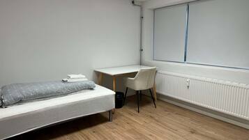 A bedroom with a bed, a desk, a chair, and a window.