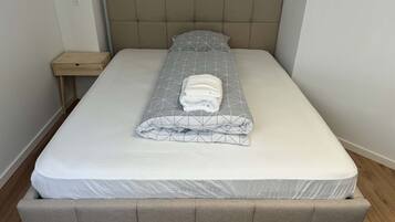 Una cama con colchón y cabecera tapizados en gris.