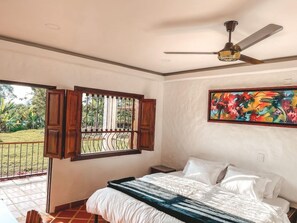 A bedroom with a bed, a ceiling fan, a window with curtains, and a painting on the wall. - Hotel Casona Montañesa Quindío (Montenegro)